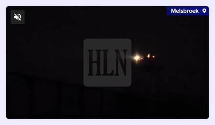 Screenshot of HLN reporter video "grote drone boven luchtmachtbasis Melsbroek": bright landing lights low over the field. 2025-11-06 shortly before 21:00 local, Melsbroek air base (next to Brussels Airport), Belgium. Status: VRT NWS Check (19 Nov 2025): the lights match a landing DHL cargo aircraft (ADS-B landing path shown). Note: Identified as a landing aircraft.